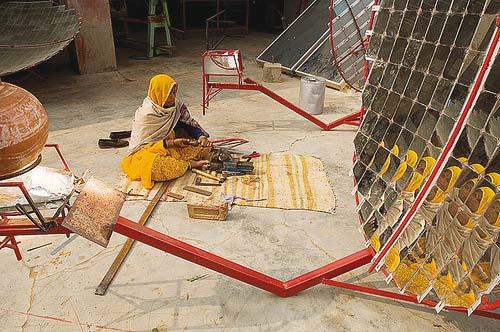 Woman in traditional attire assembling parts of a large solar reflector on the ground, surrounded by tools.