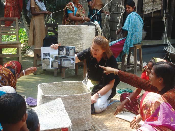 Woman showing a booklet with craft examples to a group of women who are weaving baskets.