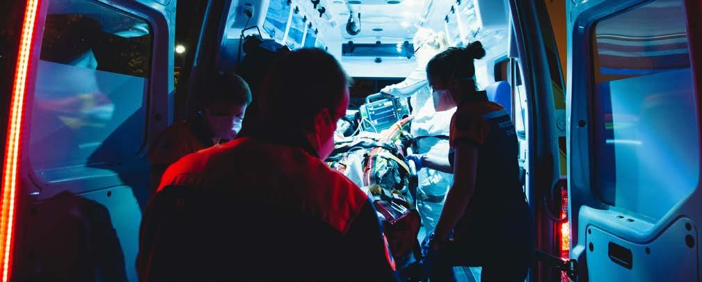 Paramedics attending to a patient on a stretcher inside a brightly lit ambulance with medical equipment visible.
