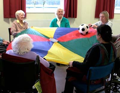 Older adults sitting in a circle, holding a colorful parachute with a soccer ball on it during an activity.