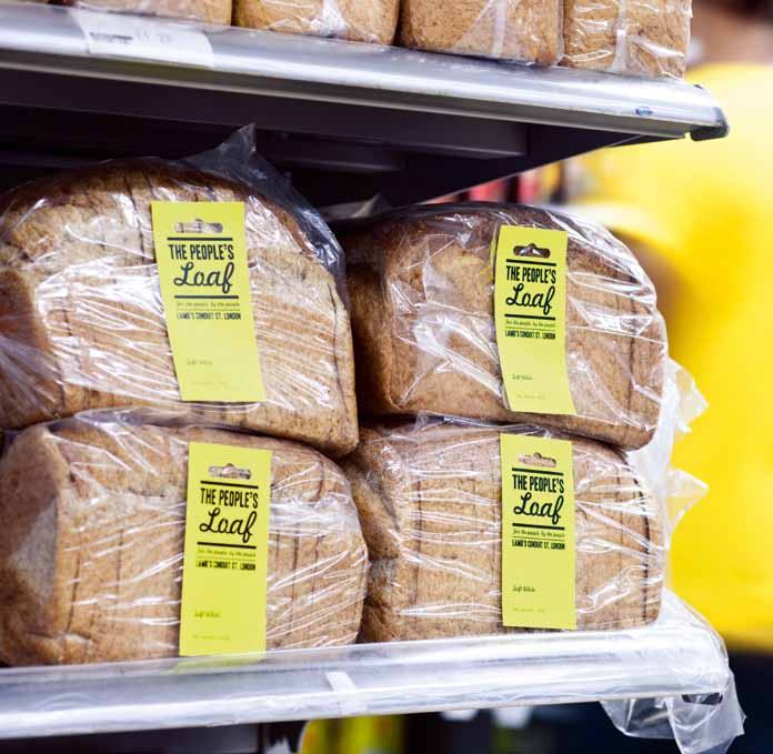 Stacked loaves of "THE PEOPLE'S Loaf" bread, individually wrapped with yellow labels, on a supermarket shelf.