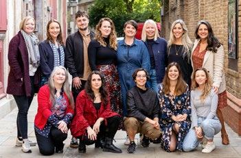 Group photo of approximately 13 diverse individuals, some standing and some kneeling, smiling outdoors.