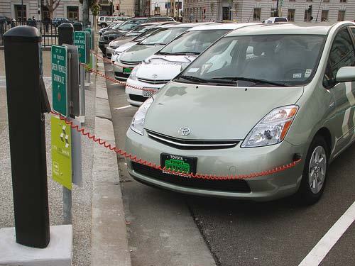 Hybrid cars charging at an outdoor station on a city street.