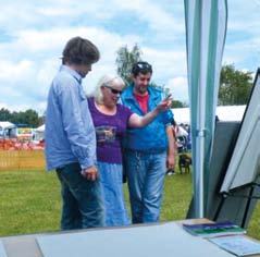 Three people, two men and a woman, looking intently at artwork displayed on an easel under a tent at an outdoor event.