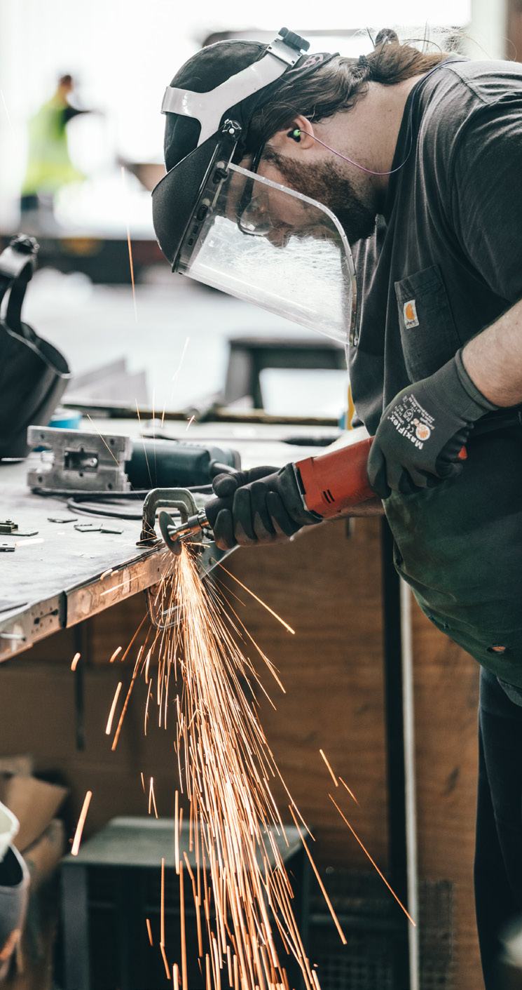 Worker wearing a face shield and gloves operating an angle grinder, creating sparks, in an industrial workshop.