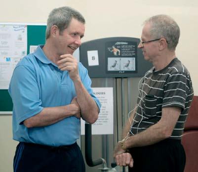 Two men talking beside exercise equipment in a gym or rehabilitation setting.