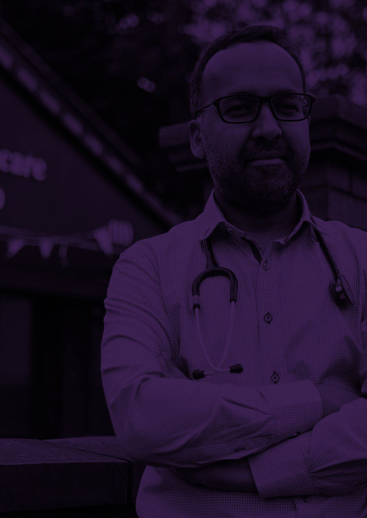 Man with a beard, glasses, and stethoscope around his neck, standing with arms crossed, with a purple overlay.