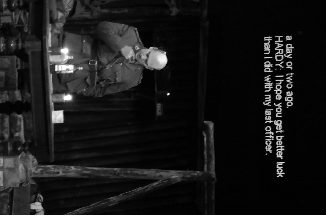 Black and white screenshot from a film showing a person in uniform sitting at a candlelit table, with overlaid dialogue stating, "HARDY: I hope you get better luck than I did with my last officer."