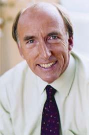Portrait of a smiling man in a light shirt and patterned tie, looking directly at the viewer.