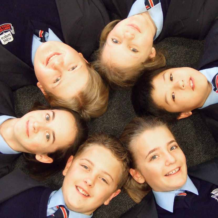 Six smiling children in school uniforms lying in a circle with their heads together.
