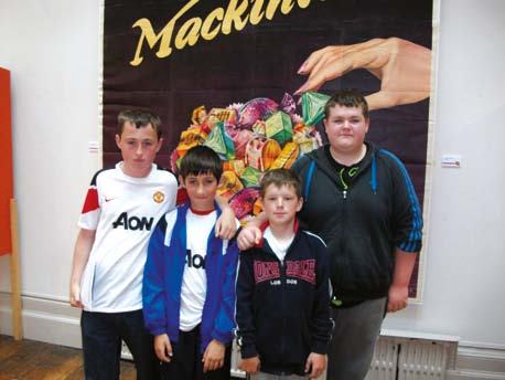 Four boys standing in front of a large poster advertising "Mackintosh's" sweets.