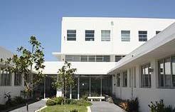 Exterior view of a white, multi-story building with a courtyard and green landscaping, possibly a hospital or clinic.
