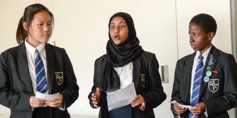 Three students in school uniforms, one wearing a hijab, actively speaking or presenting during an event.