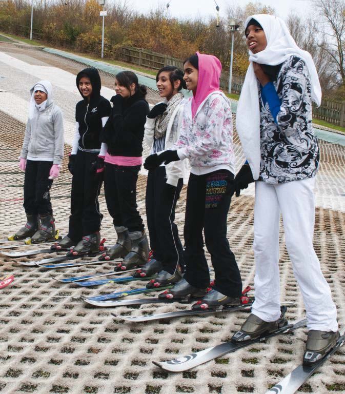 Group of young women, some in hijabs, standing on skis on a dry ski slope.