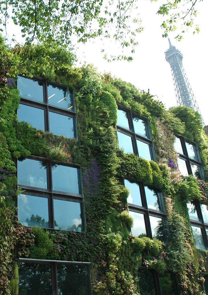 Building with a lush green vertical garden, partially obscuring windows, with the top of the Eiffel Tower visible in the background.