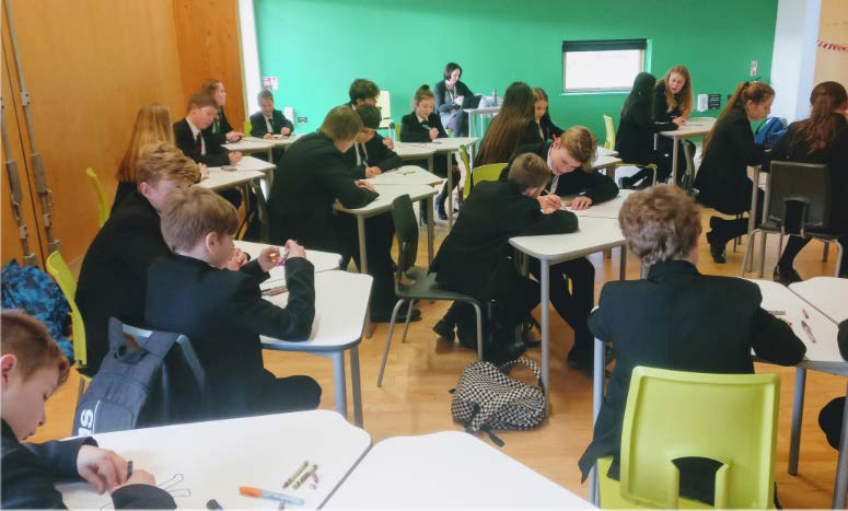 A wide shot of a classroom filled with students in uniform seated at individual desks, engaged in learning activities.