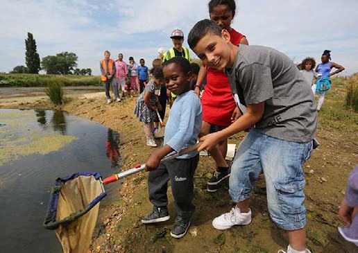 Two boys hold a net by a pond while other children and adults stand nearby, participating in a park activity.