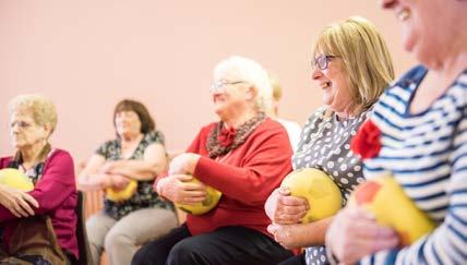 Senior women smiling while participating in a group exercise activity, each holding a yellow ball.