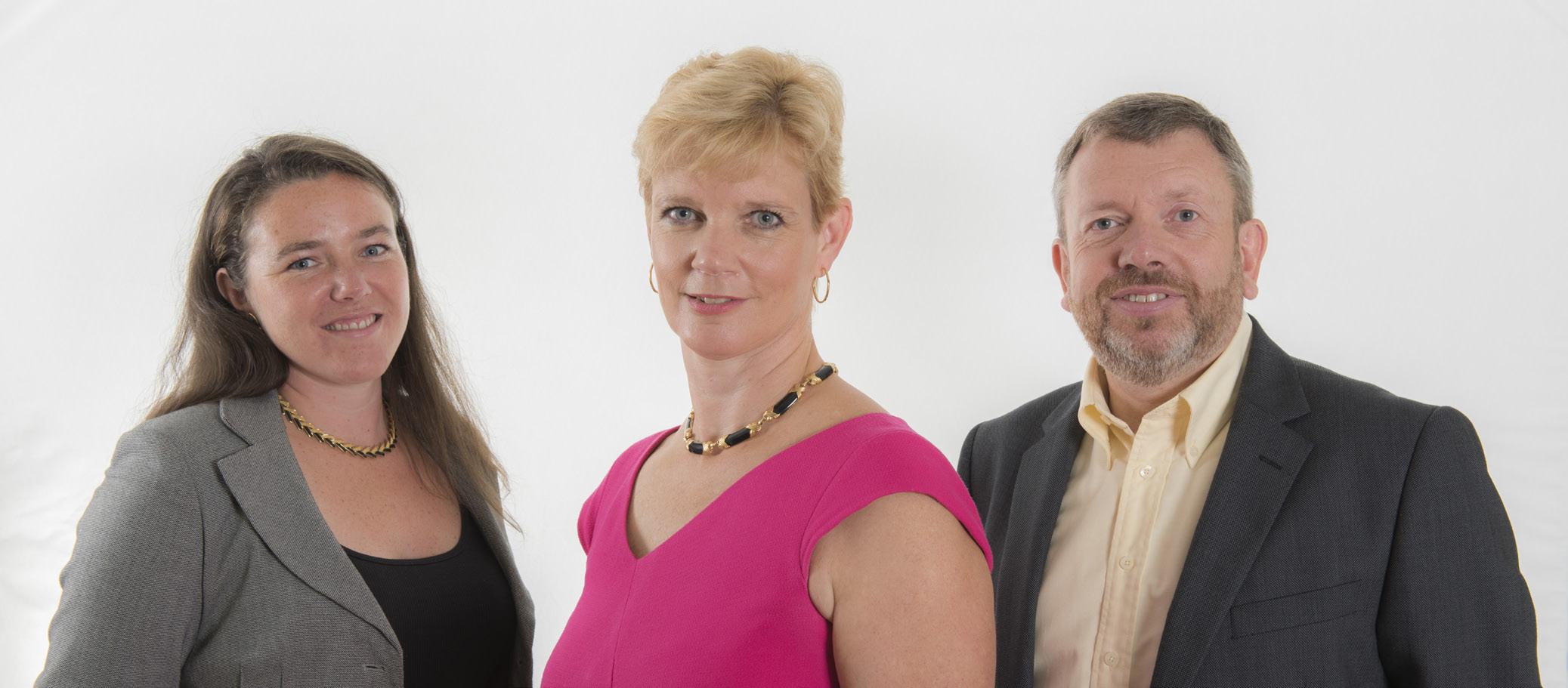 Group photo of three smiling people, two women and one man, posing in front of a white background.