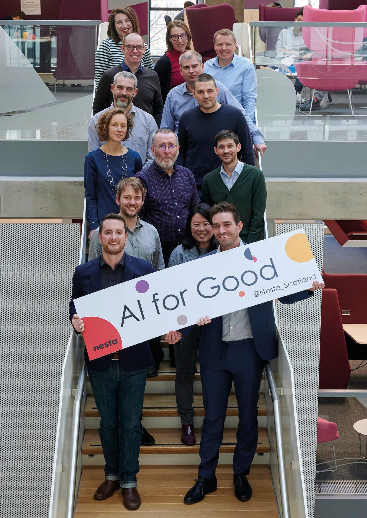 Group photo of a team on a staircase, with two men in front holding an "AI for Good" sign by Nesta Scotland.