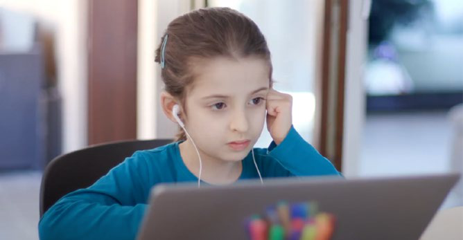 Young girl with earphones concentrates while looking at a laptop screen, illustrating remote learning or digital engagement.
