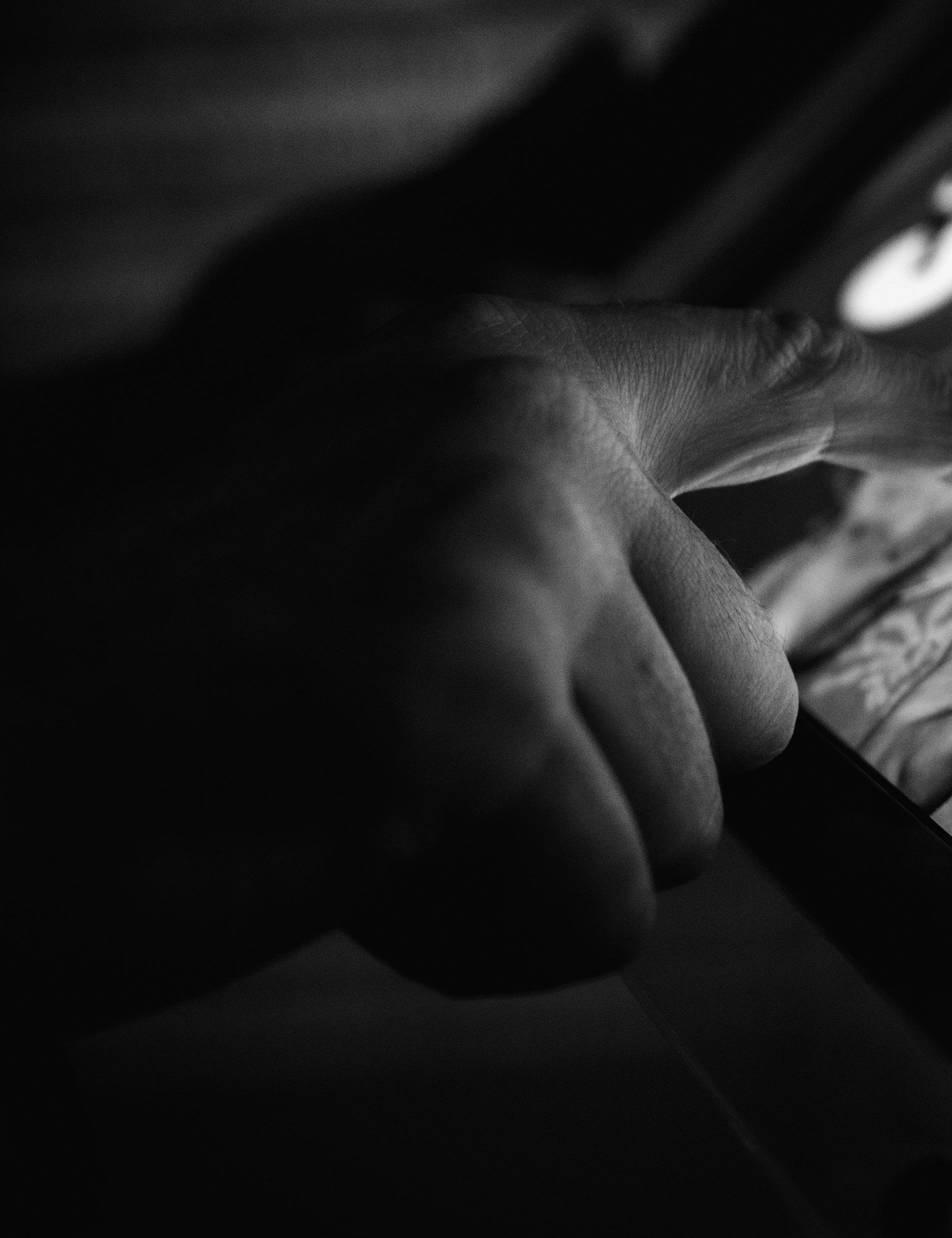 Close-up black and white photo of a person's hand holding and interacting with a smartphone, showing a subtle screen glow.