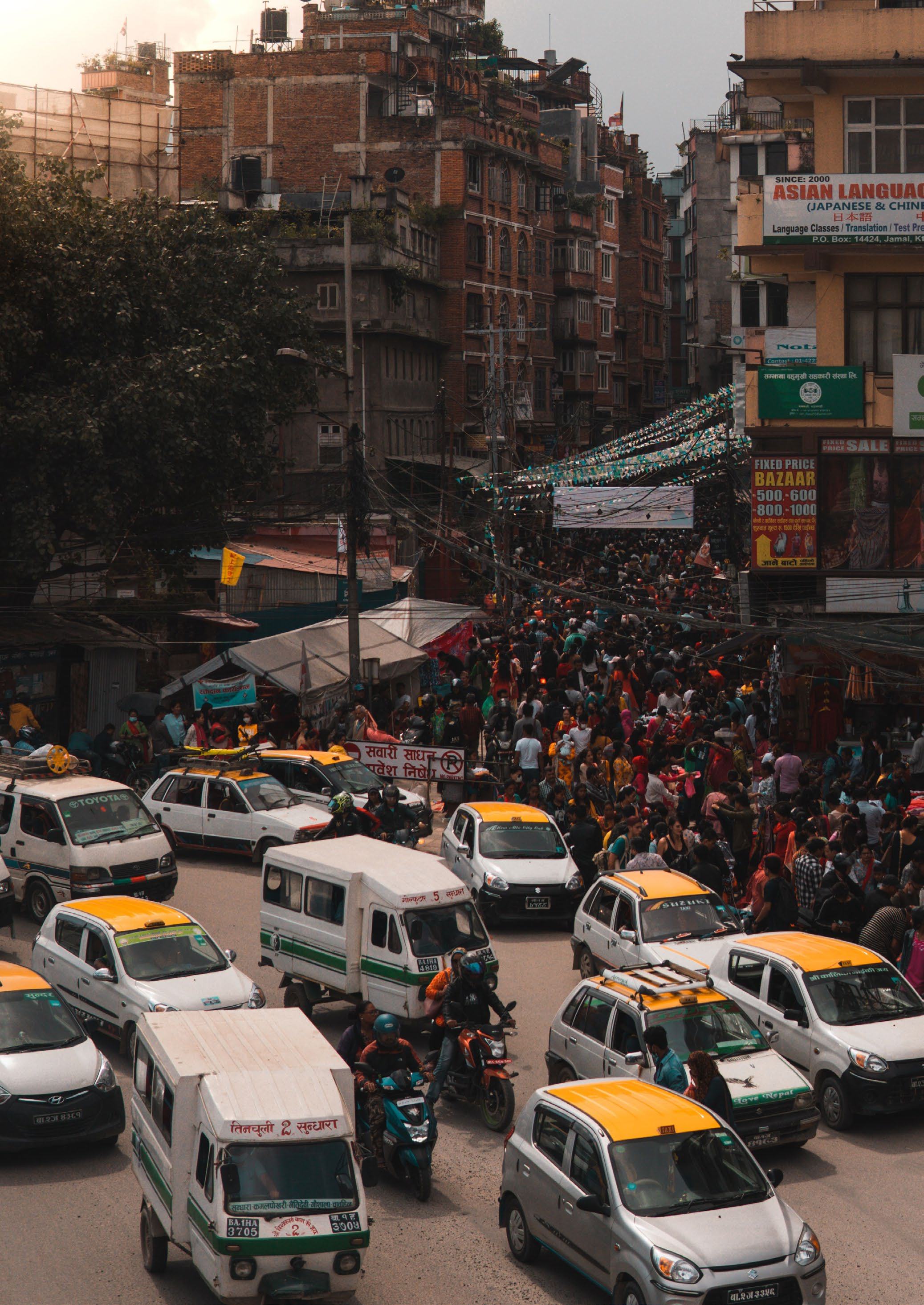 Busy street scene in a city with many cars, motorcycles, and pedestrians amidst buildings.