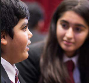 Two students in uniform, a male and a female, look at each other, engaged in conversation or interaction.