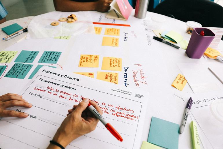 Close-up of hands writing on a document titled "Problema y Desafío" (Problem and Challenge) surrounded by brainstorming sticky notes, capturing a content creation process.