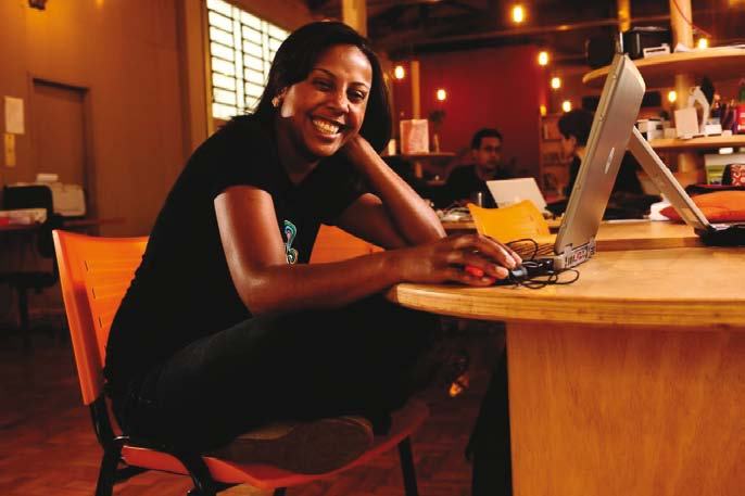 Smiling woman sitting at a desk using a laptop and mouse in a modern office environment.