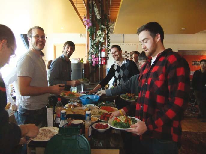 Group of people serving themselves food from a buffet table at a social gathering.