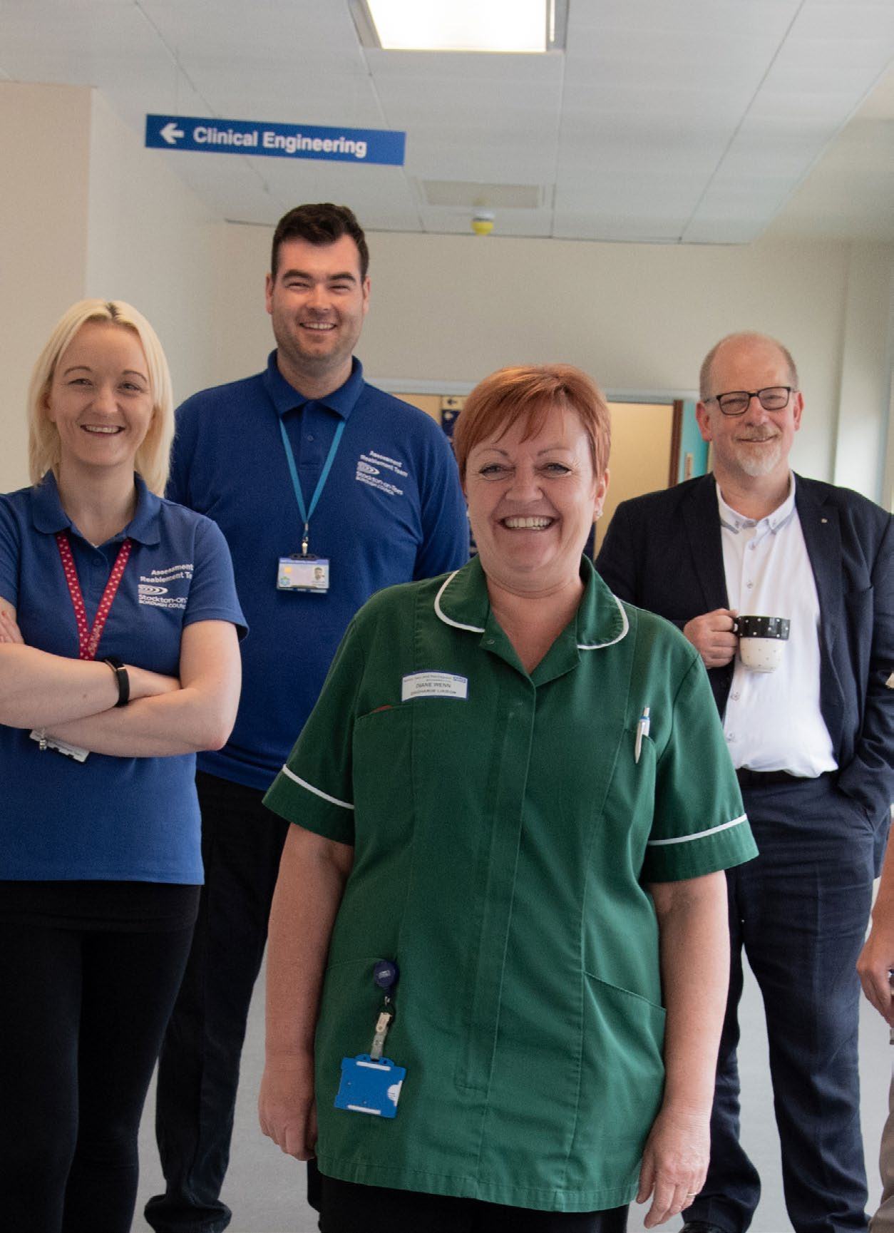 Four smiling individuals, two women and two men, in a hospital hallway with a Clinical Engineering sign.