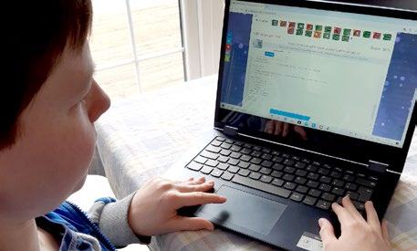 Young person looking at a laptop screen showing a programming interface with colorful blocks and text, likely engaged in an educational coding activity.
