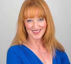 Headshot of a smiling woman with long red hair and a blue top.