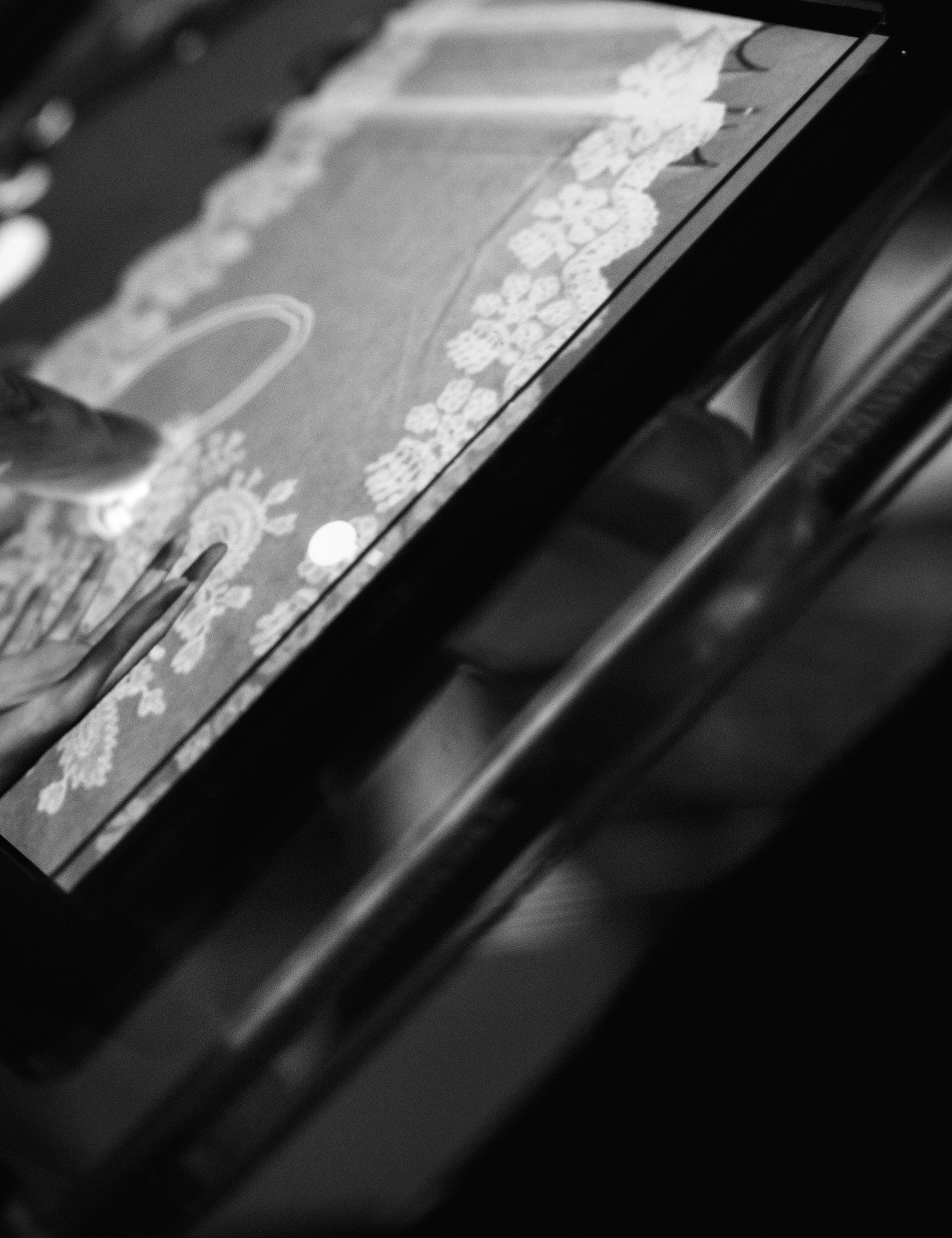 Angled black and white close-up of a hand touching an interactive screen or surface displaying intricate patterns.