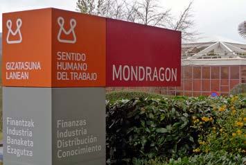 Signpost for Mondragon, displaying company name, values (Human Sense of Work), and business areas (Finance, Industry, Distribution, Knowledge) in Basque and Spanish.