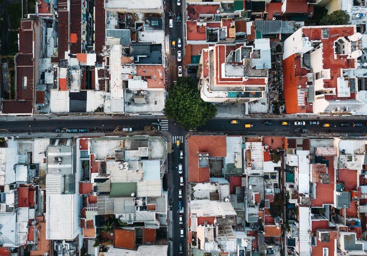 Aerial view of a dense urban area with buildings, streets, cars, and a large tree at an intersection