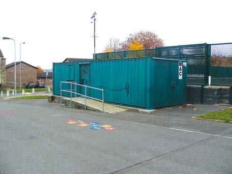 A green modular container building with a ramp and a "MAC" label, located next to an outdoor fenced area.