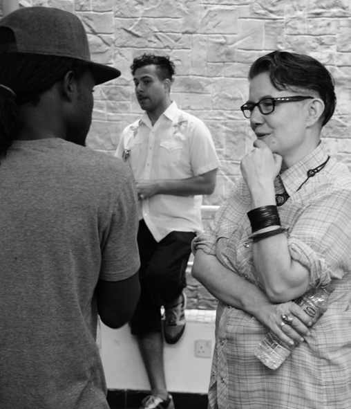 A candid black and white photo of three people, two of whom appear to be in conversation or discussion, with one woman listening intently.