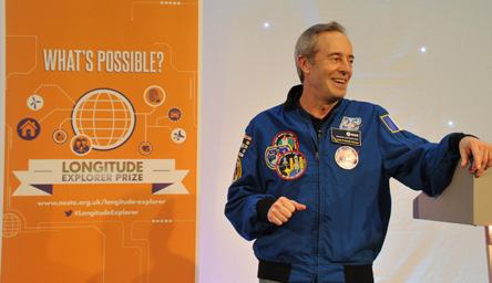 An astronaut next to an infographic banner for the Longitude Explorer Prize, featuring a globe connected to icons representing innovation and problem-solving.