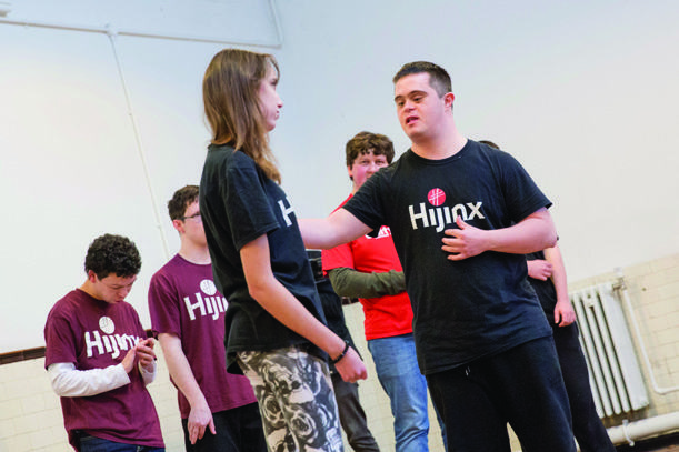 A group of young people, some with Down syndrome, interact in a room, possibly rehearsing or engaged in a workshop.
