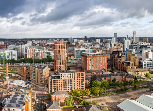 Aerial view of a city skyline with numerous buildings, roads, and a cloudy sky.