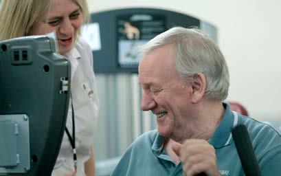 An older man smiling while using an exercise machine, with a woman smiling behind him.