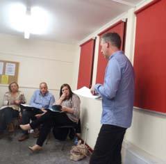 A man standing and giving a presentation or leading a discussion to a small group of people seated in a meeting room.