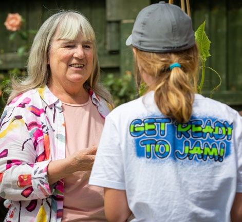 An older woman talking to a younger person in a 'Get Ready to Jam!' t-shirt in an outdoor setting.