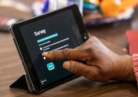 Close-up of a hand interacting with a tablet displaying an online survey with sliders for voting on topics like investment in social housing and community energy.