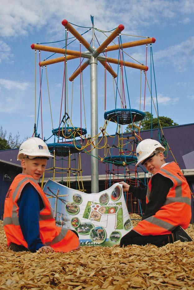 Two boys in hard hats and safety vests holding a map in front of a colorful playground structure.
