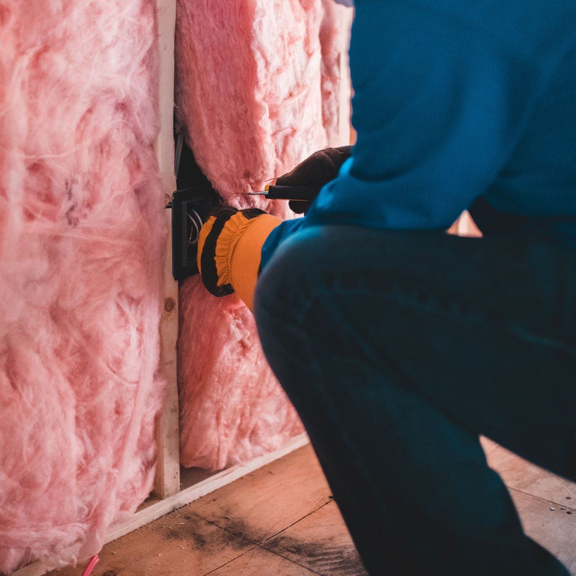 Worker installing pink fiberglass insulation between wall studs, demonstrating a home energy efficiency improvement process.