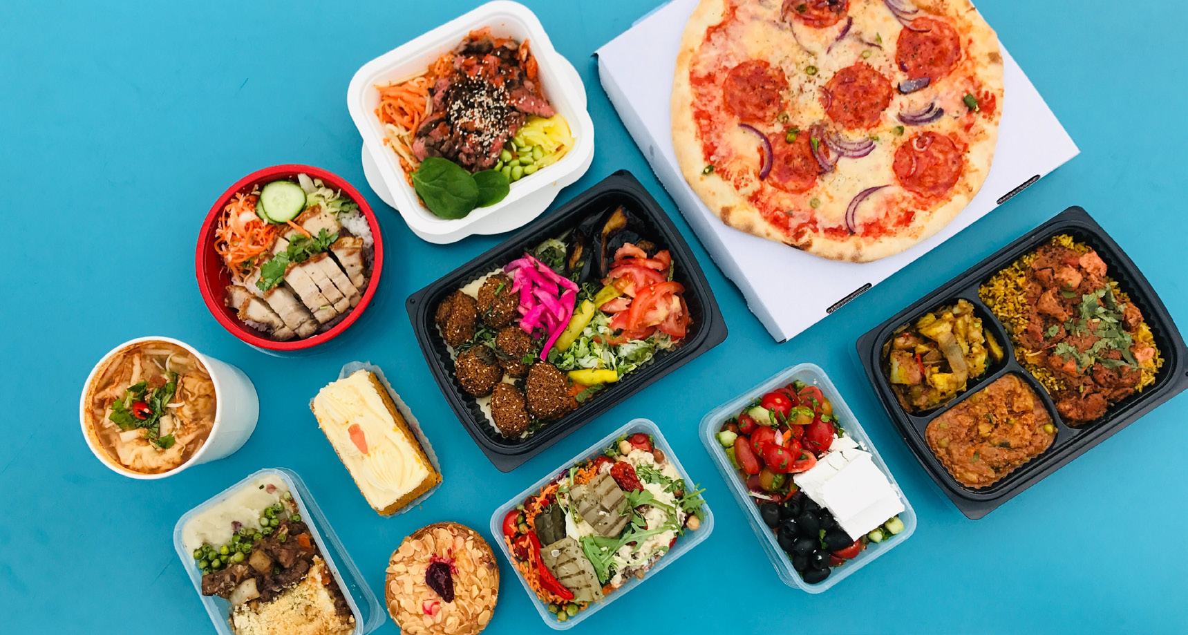 Overhead view of a variety of takeout food containers including pizza, salads, and main dishes on a blue background.