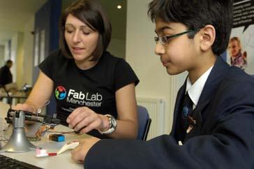 A woman helps a young boy assemble electronic components in a hands-on learning environment.